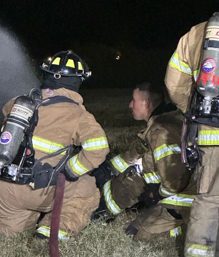 A group of firefighters are kneeling down in the grass