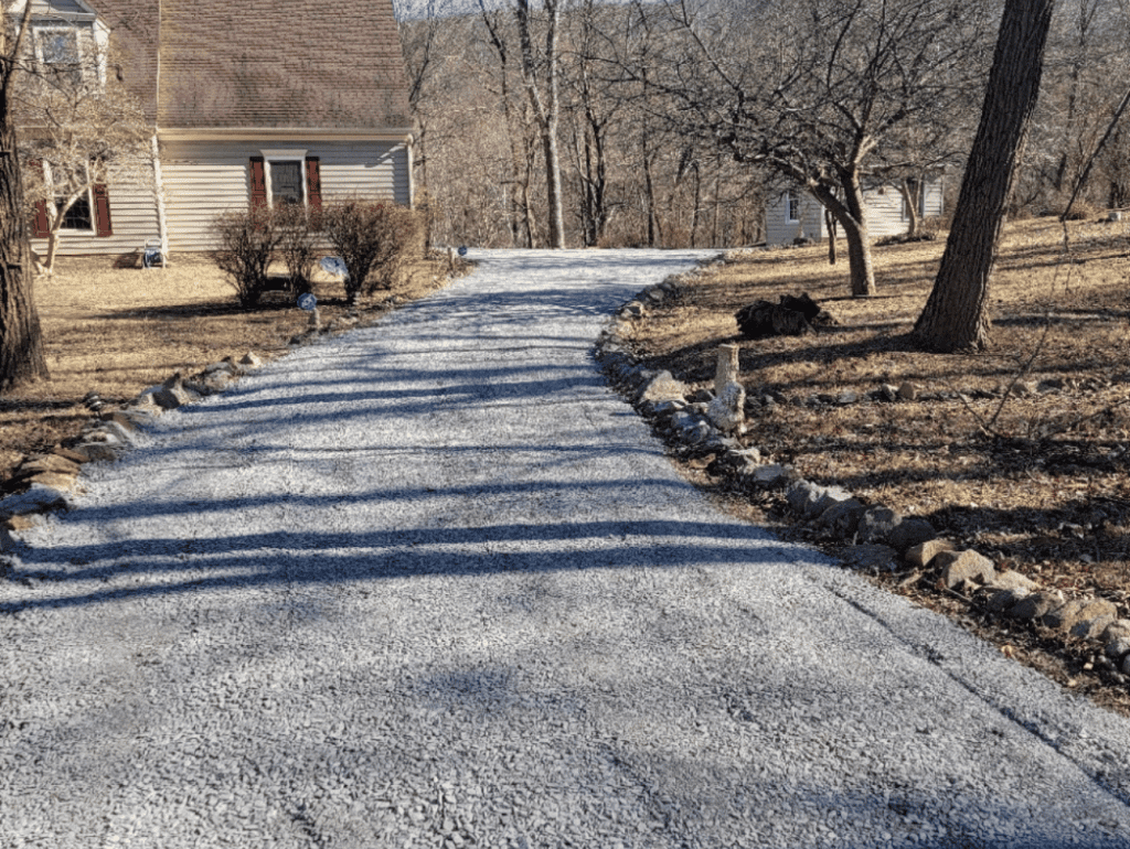 A gravel driveway leads uphill toward a house, bordered by rock edging and trees.