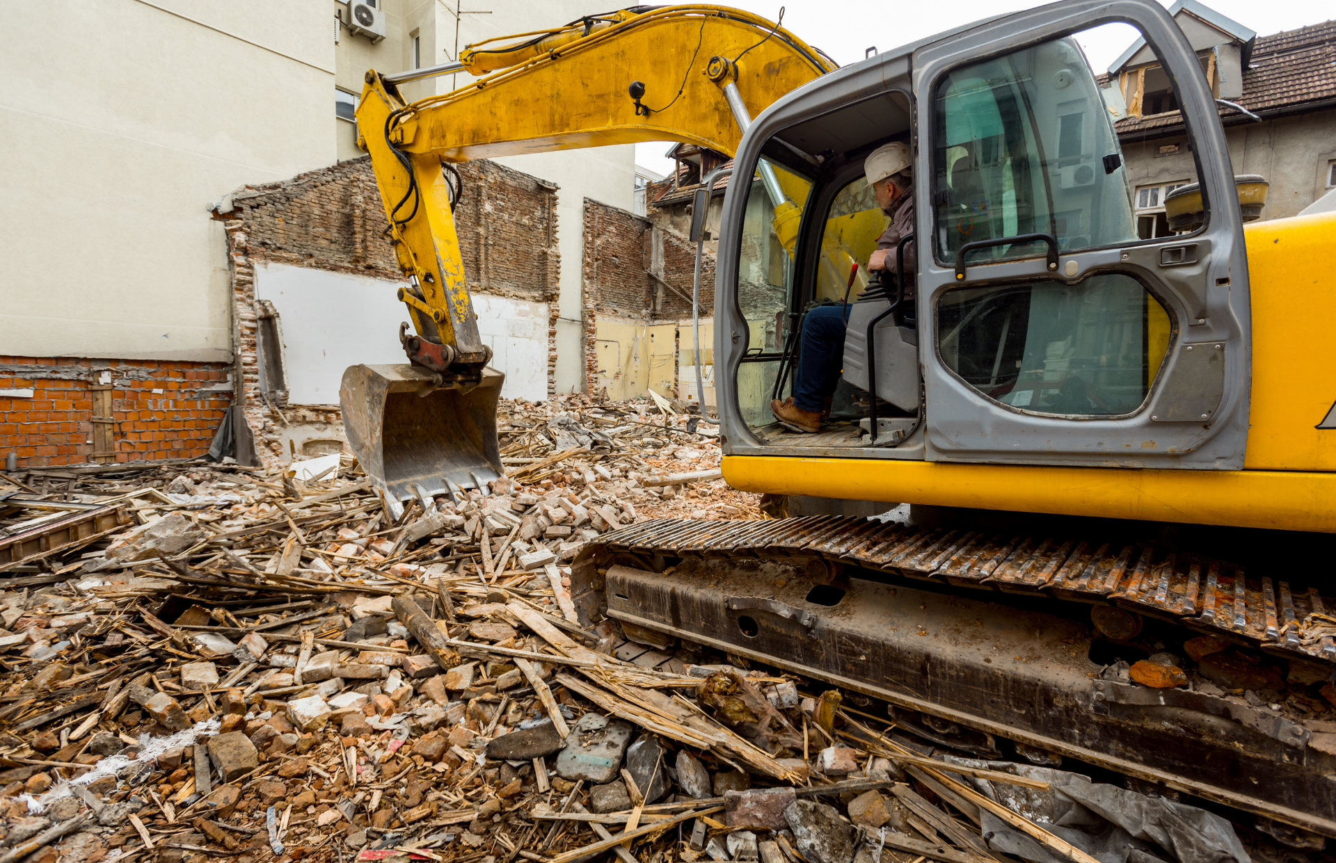 Yellow excavator demolishing a building; debris scattered around the site.