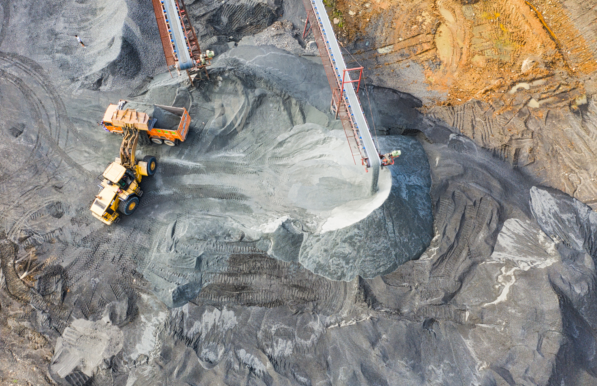 Overhead view of a quarry with construction vehicles loading material onto a conveyor belt.