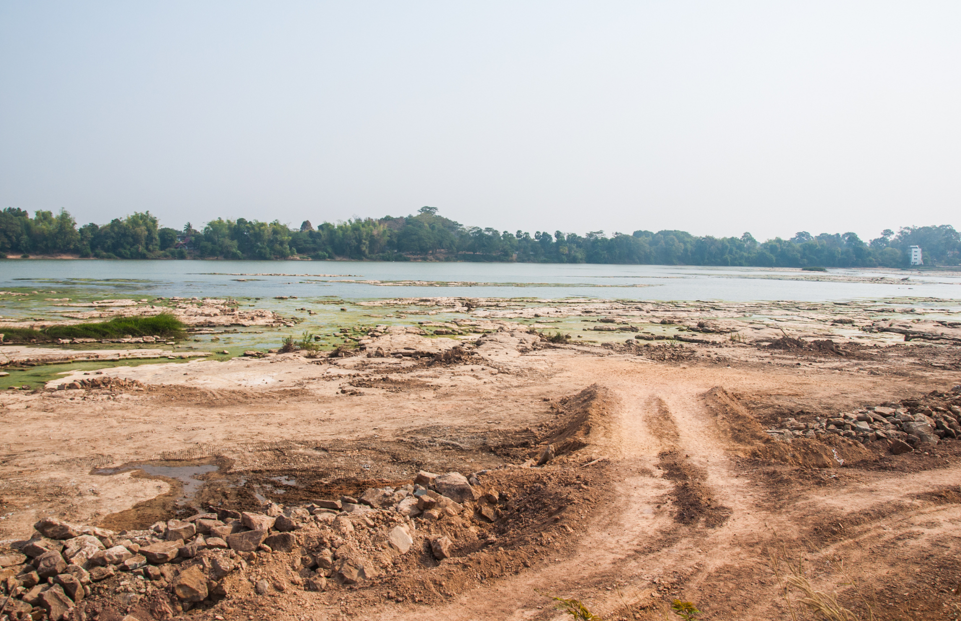 Erosion-scarred landscape with deep gullies and brown earth under a cloudy sky, with sparse trees in the background.