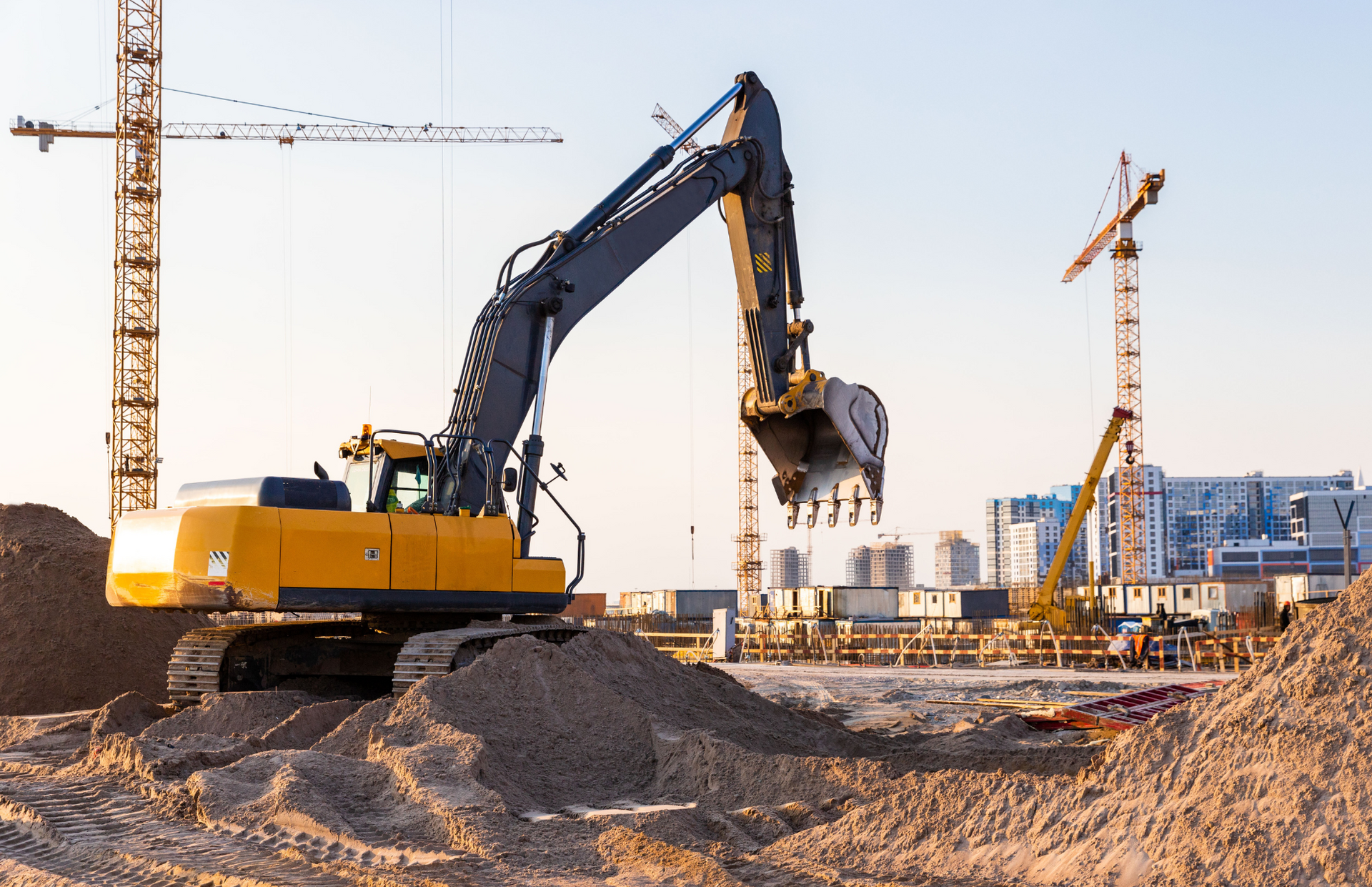 Yellow front-end loader at a construction site, moving piles of golden-colored material.