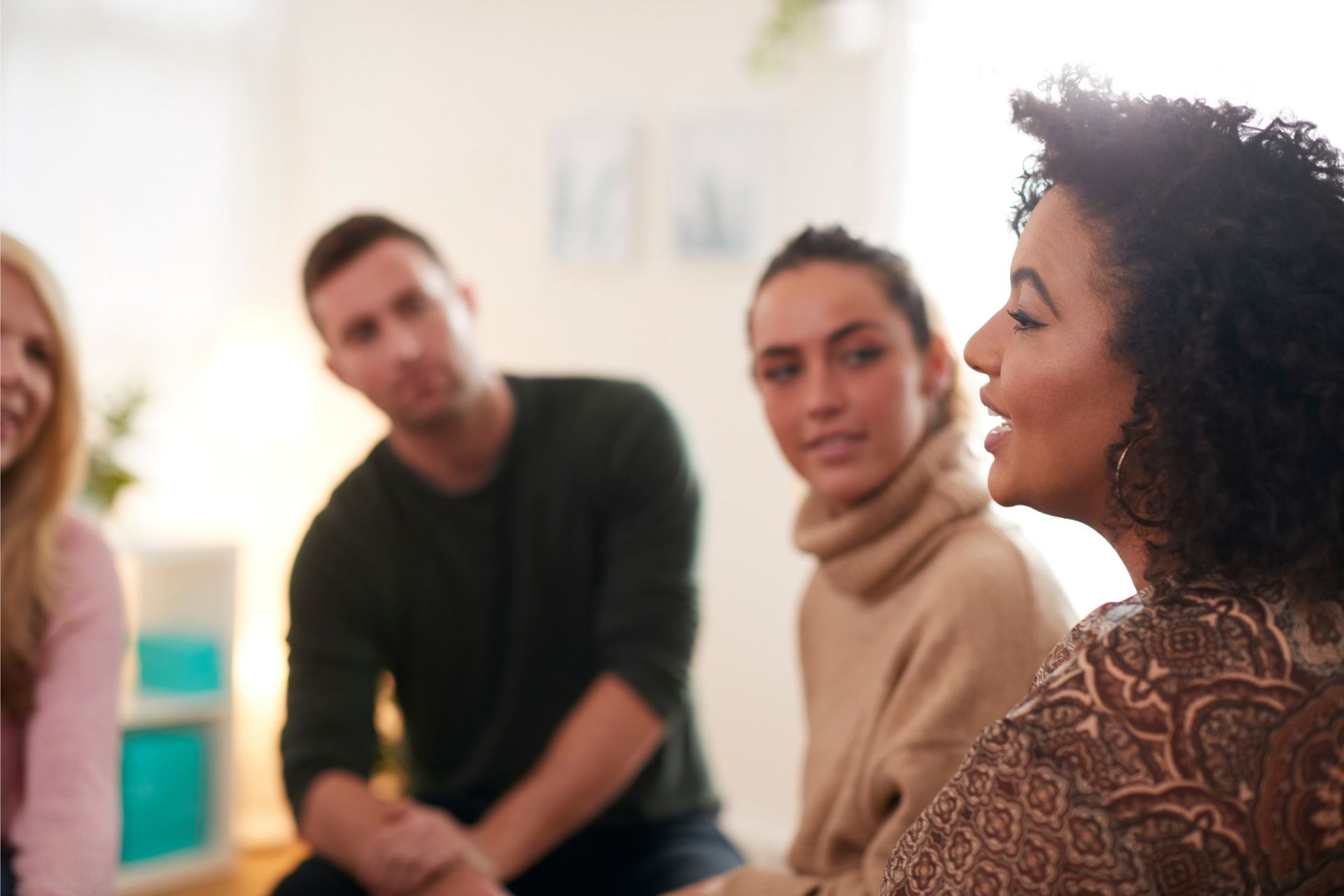 People in a circle, one speaking. Natural light fills the room.