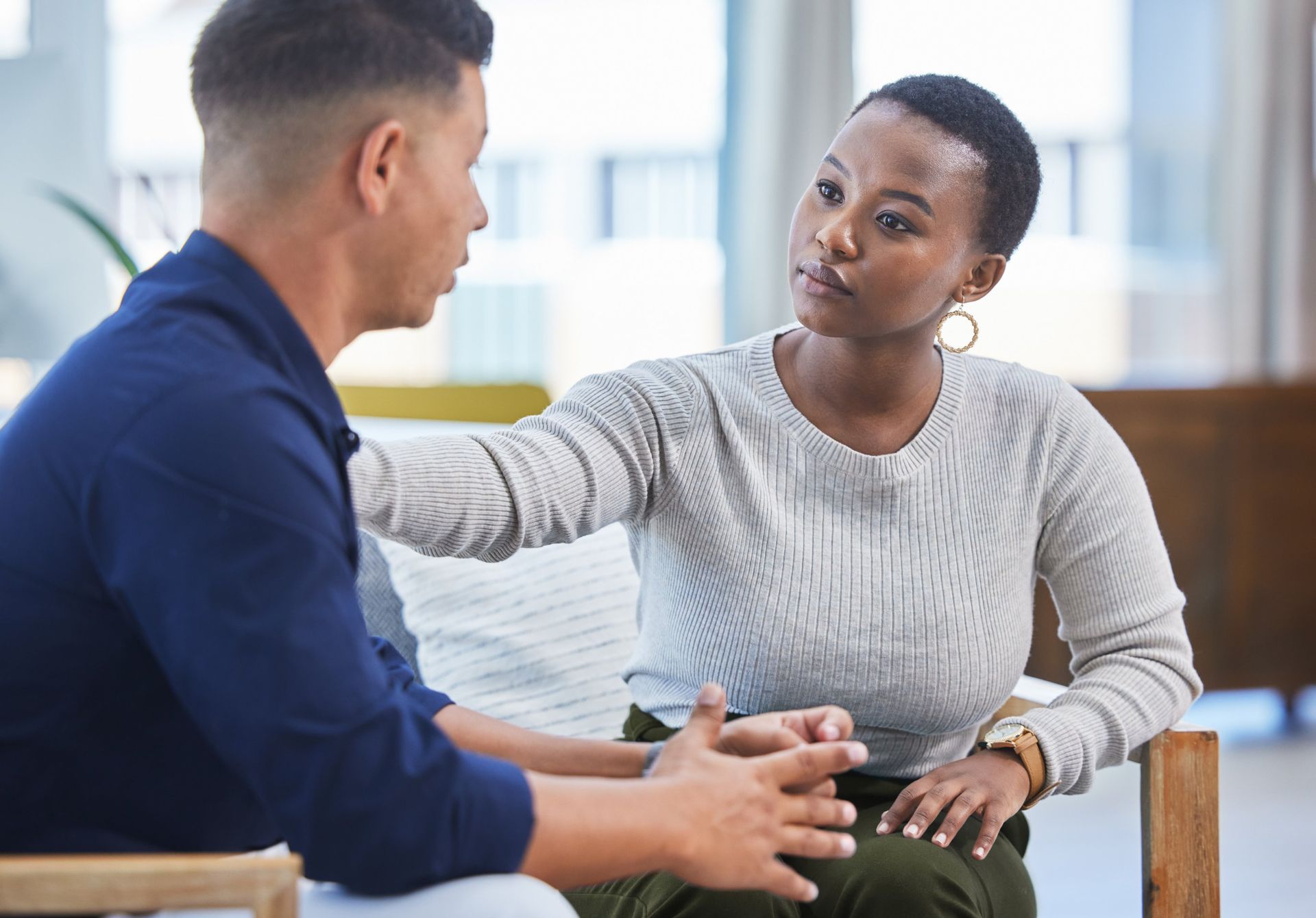 Woman consoling a person. She has hand on his shoulder and they appear to be in a therapy session.