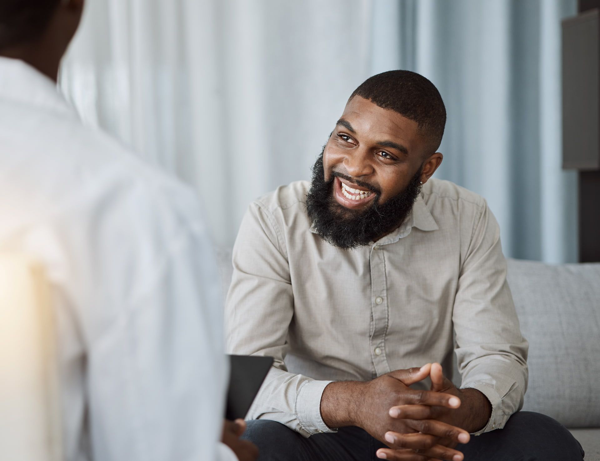 Man smiling while talking to another person in a light-filled room.