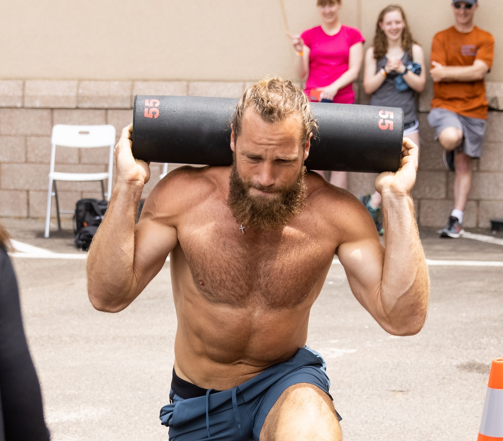 A shirtless man with a beard is carrying a black bag with the number 35 on it