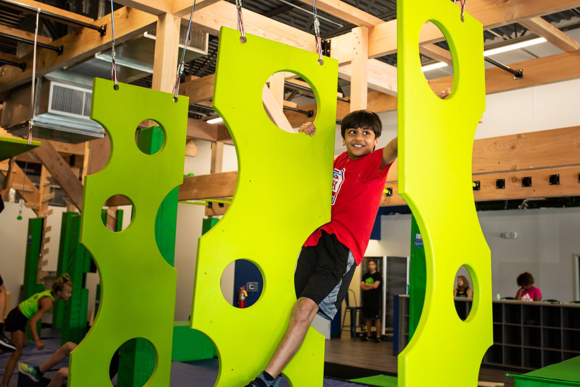 Boy climbing a lime green structure with circular holes at an indoor adventure park.