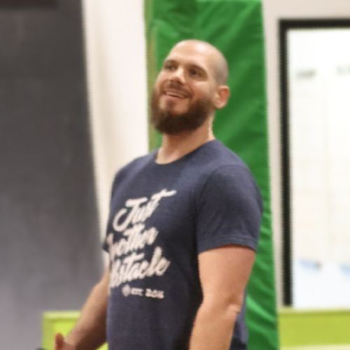 A man with a beard is wearing a shirt that says just another obstacle