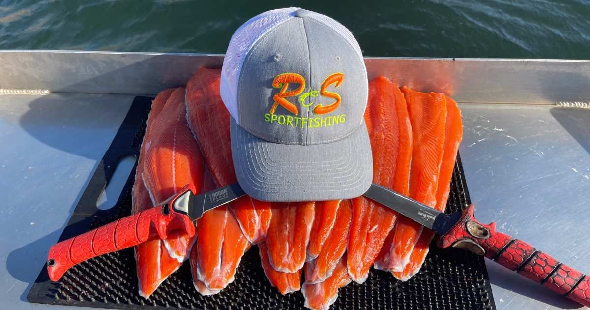 Two large fish on a tray beside a blue cap on a dock.
