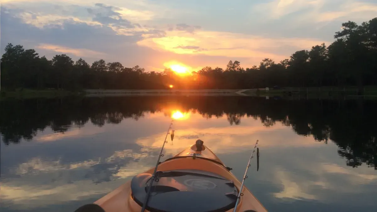 Kayak on a calm lake at sunset, with trees silhouetted along the shoreline and reflected in the water