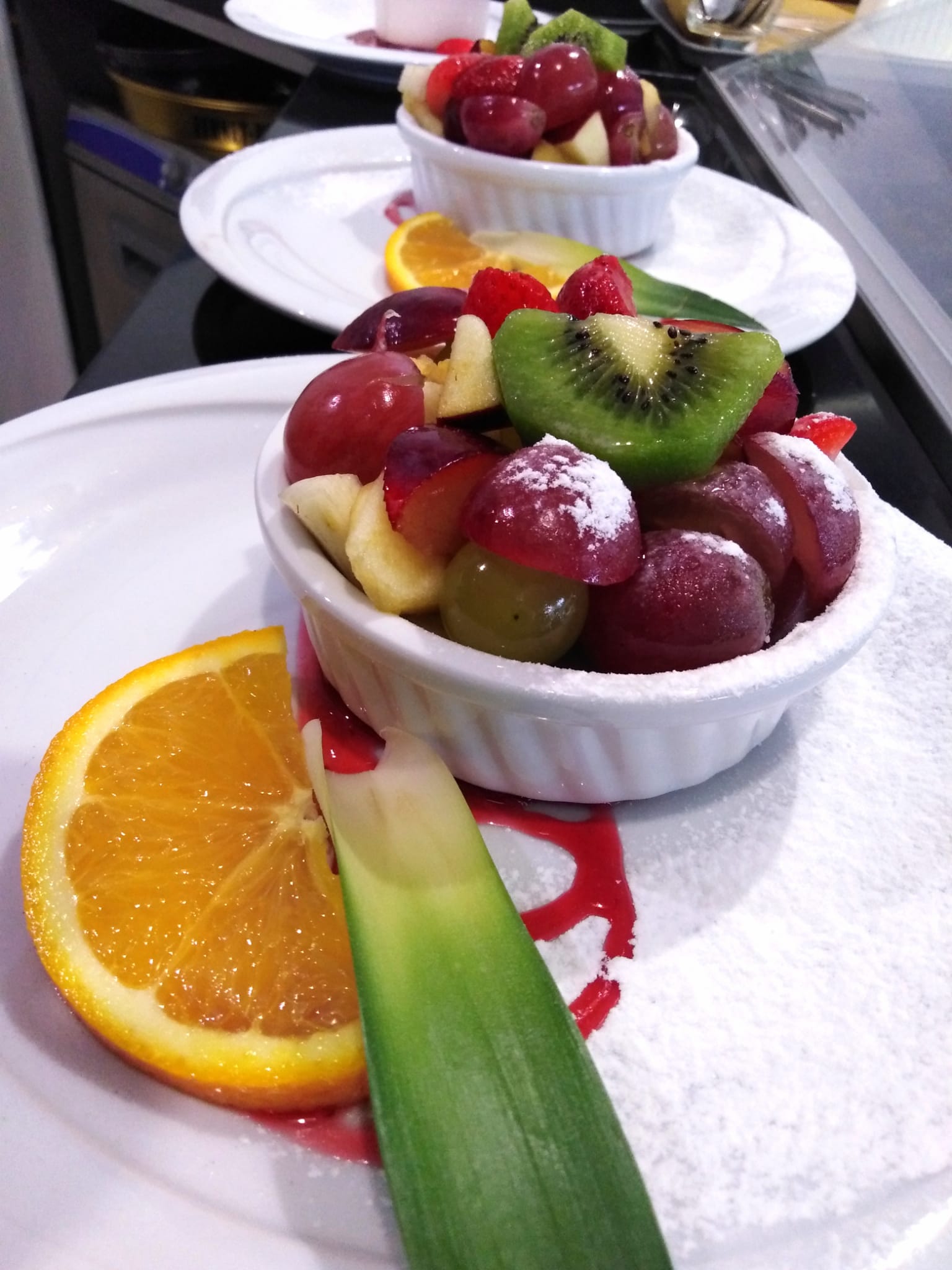 Un piatto bianco sormontato da una ciotola di frutta e una fetta d'arancia