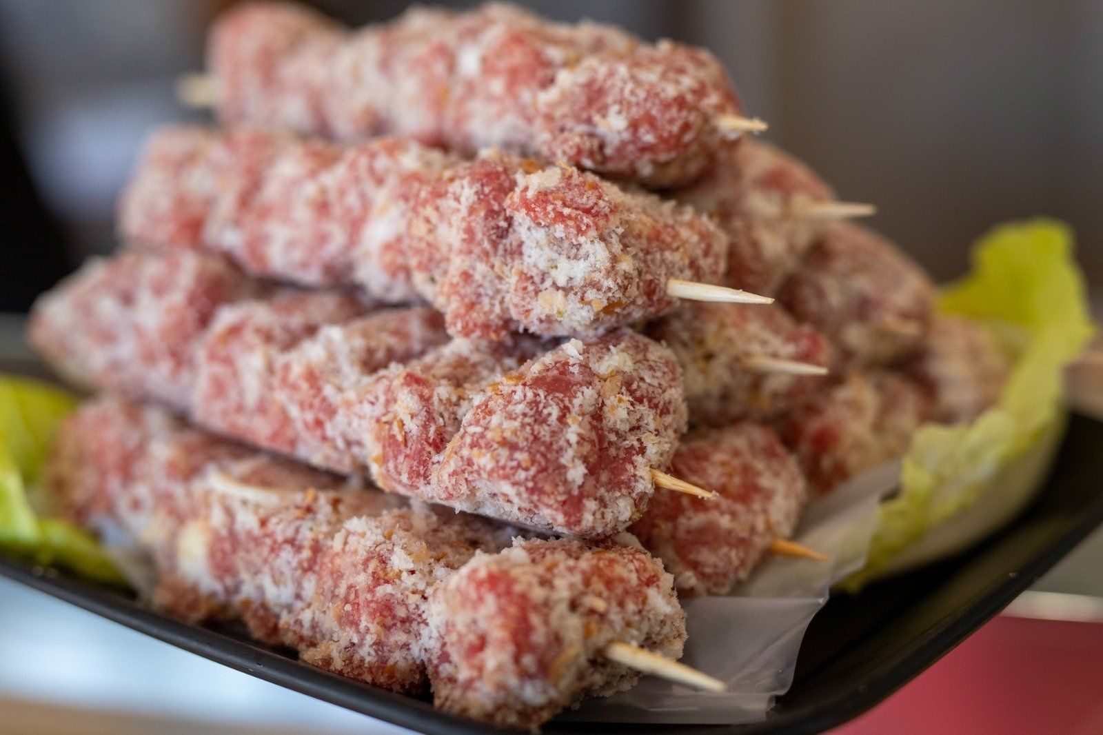 Una persona tiene in mano un vassoio di carne infilzata su degli spiedini.