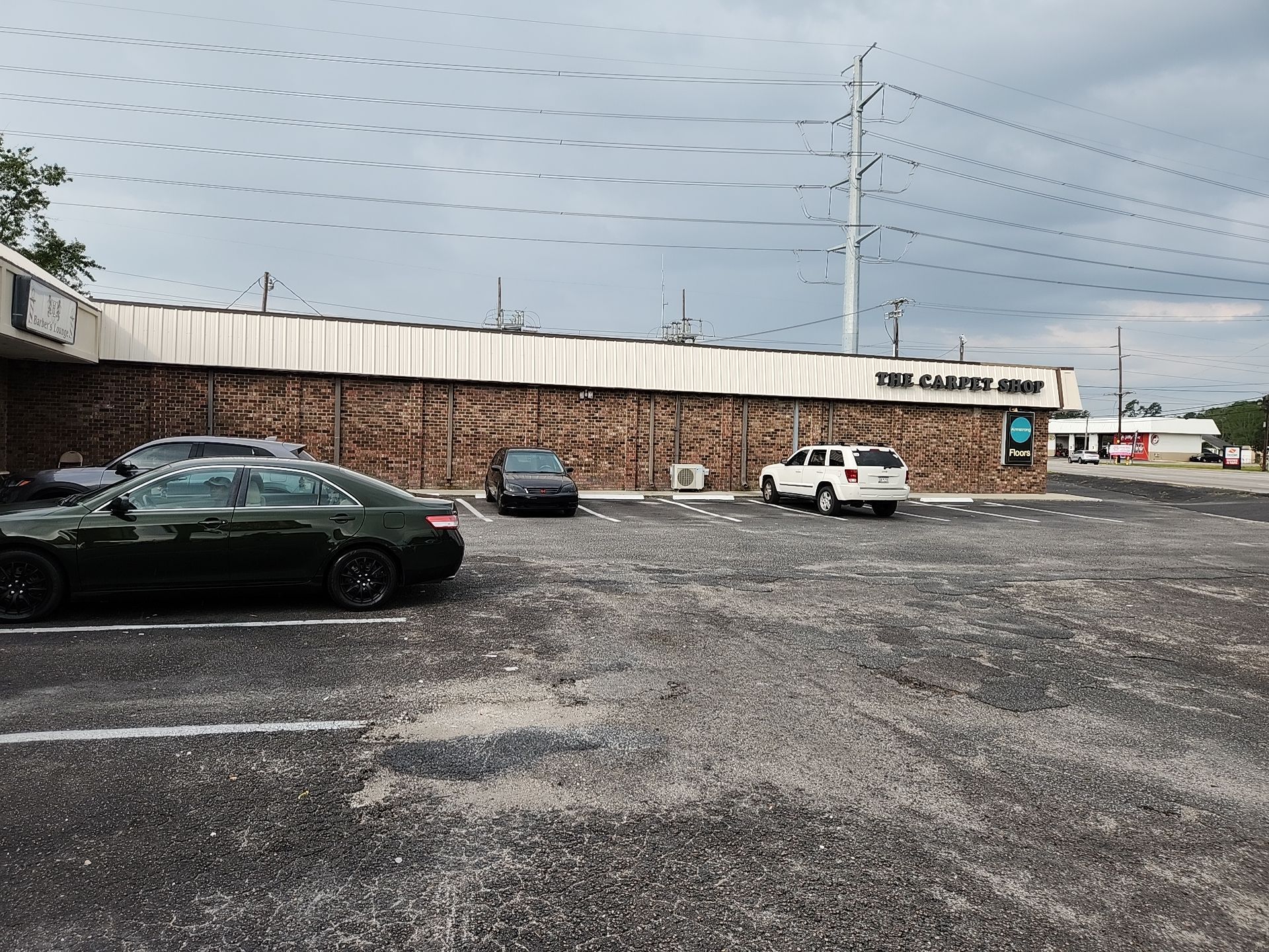 A parking lot in front of a long, single-story brick commercial building under a cloudy sky.