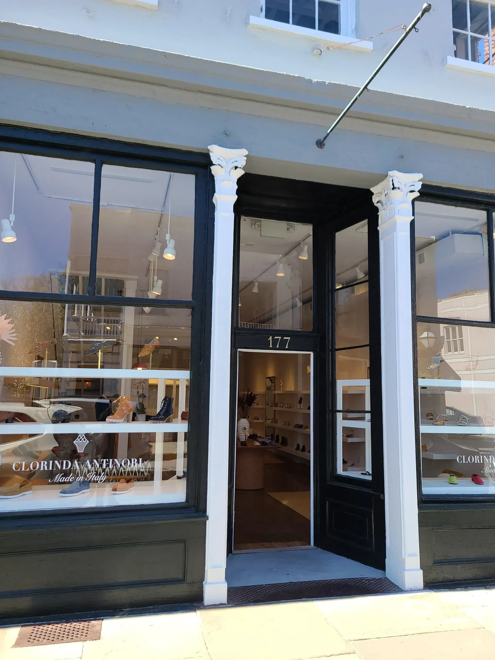 Storefront with black-framed windows, a central open door, and white columns on a city sidewalk.