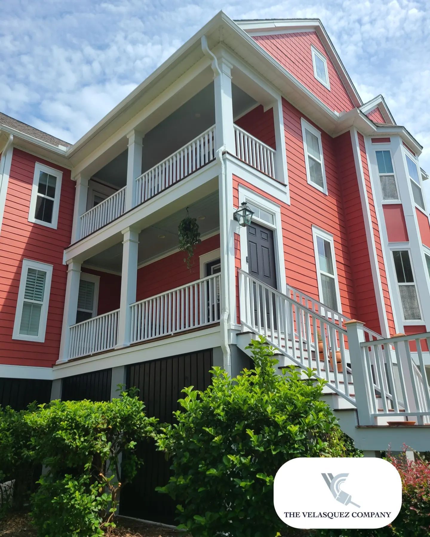 A two-story red house with white trim, featuring double-decker porches and a staircase leading to the front door.