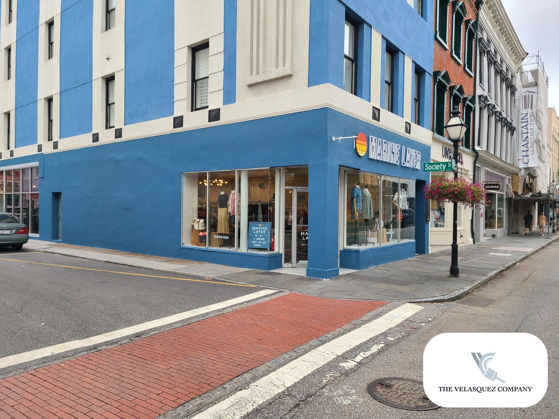 A blue corner storefront on a street with a brick crosswalk and a street lamp, under an overcast sky.