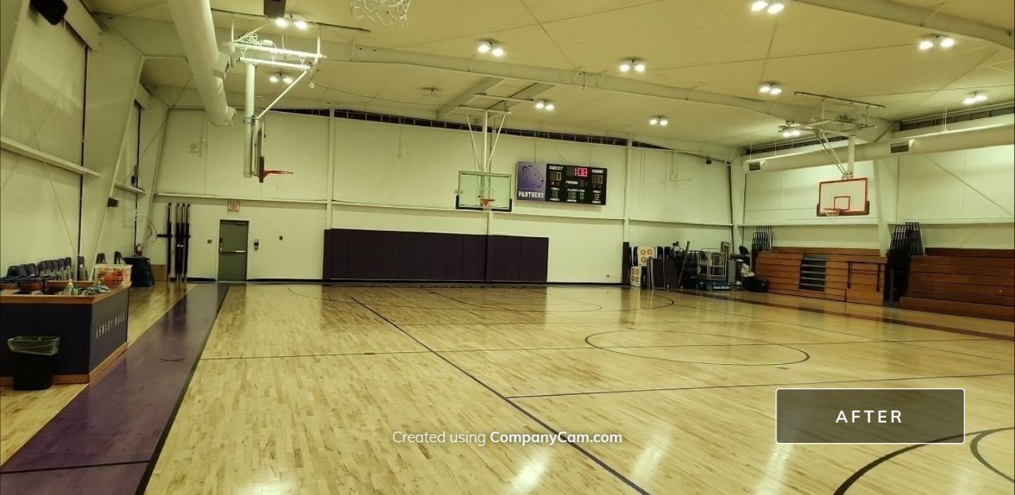 An empty indoor basketball court with wooden floors, hoops, and bleachers, labeled as