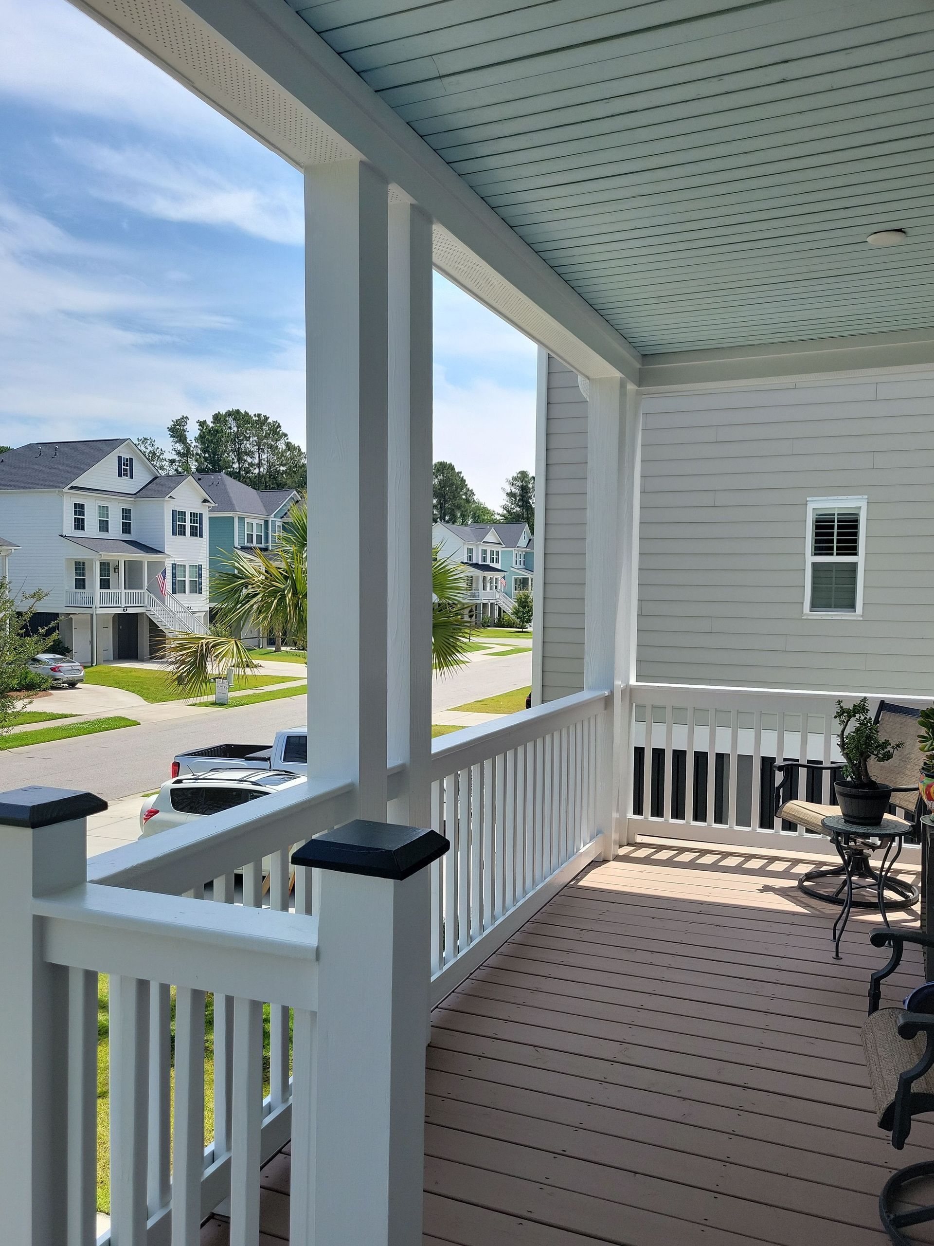 A view from a covered porch looking out at a residential street with houses on a sunny day.