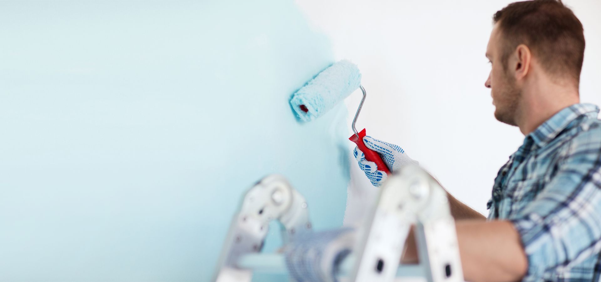 A blue house exterior with a window covered in plastic sheeting during painting work Professional painter rolling light blue paint onto an interior wall during a residential painting project