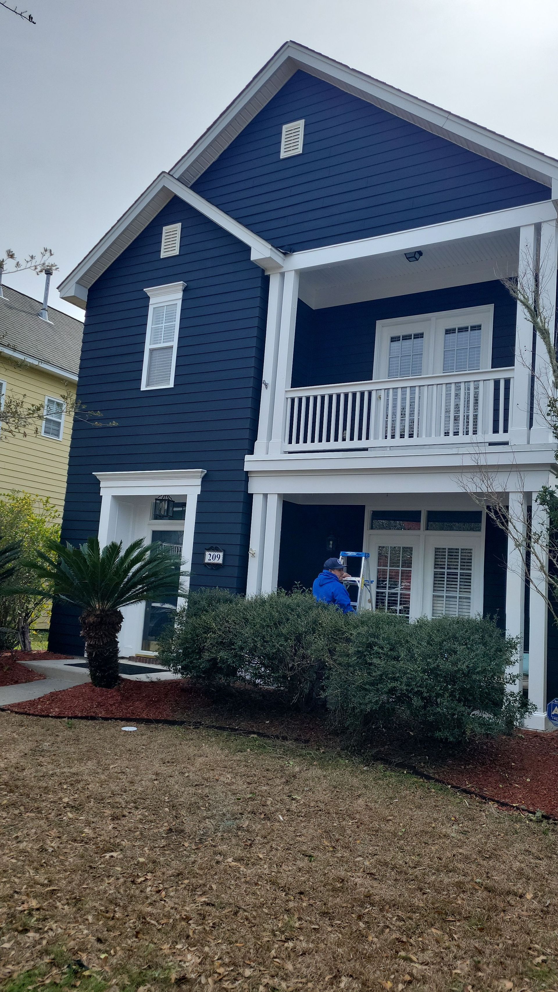 A navy blue, two-story house with a front porch, a balcony above, white trim, and a person standing in the doorway.