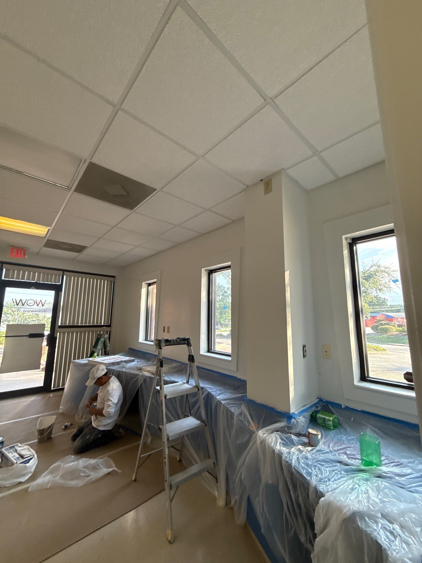 Professional painter applying white paint to wall with roller in modern bright office interior.