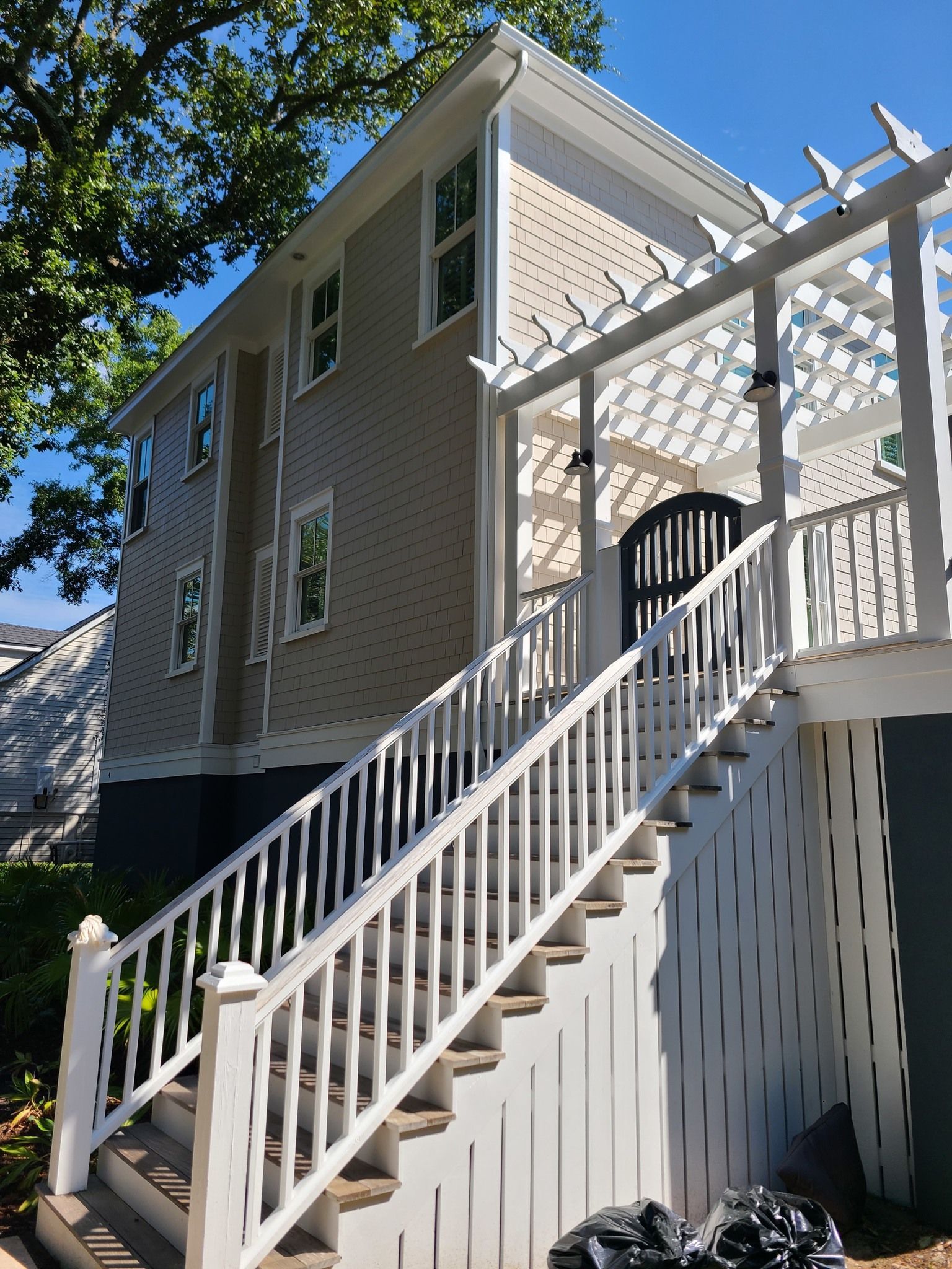 A house exterior with beige siding, a dark blue foundation, and white stairs leading to an elevated deck with a pergola.