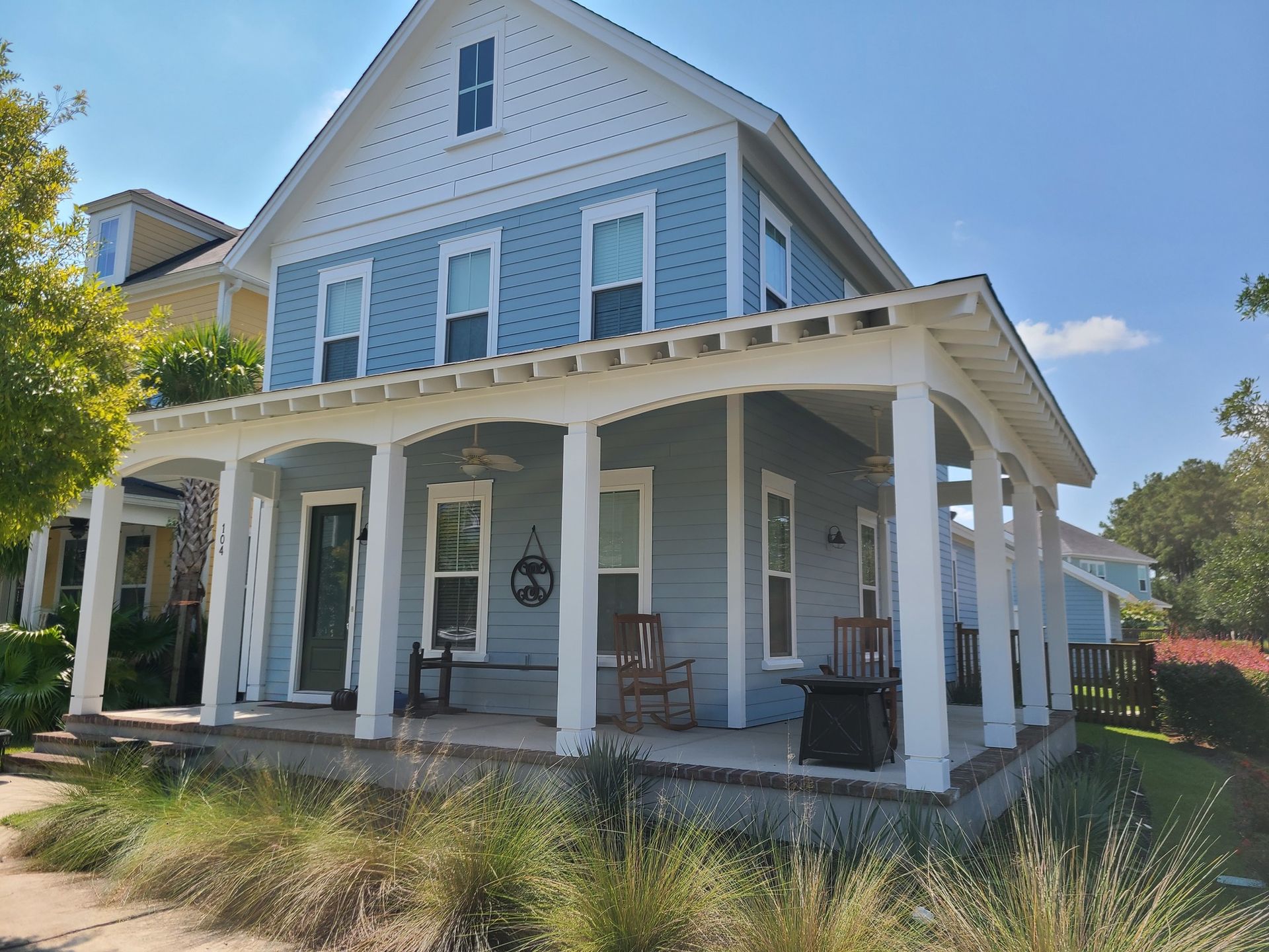A light blue two-story house with white trim, a large front porch featuring white pillars, and a green front door.