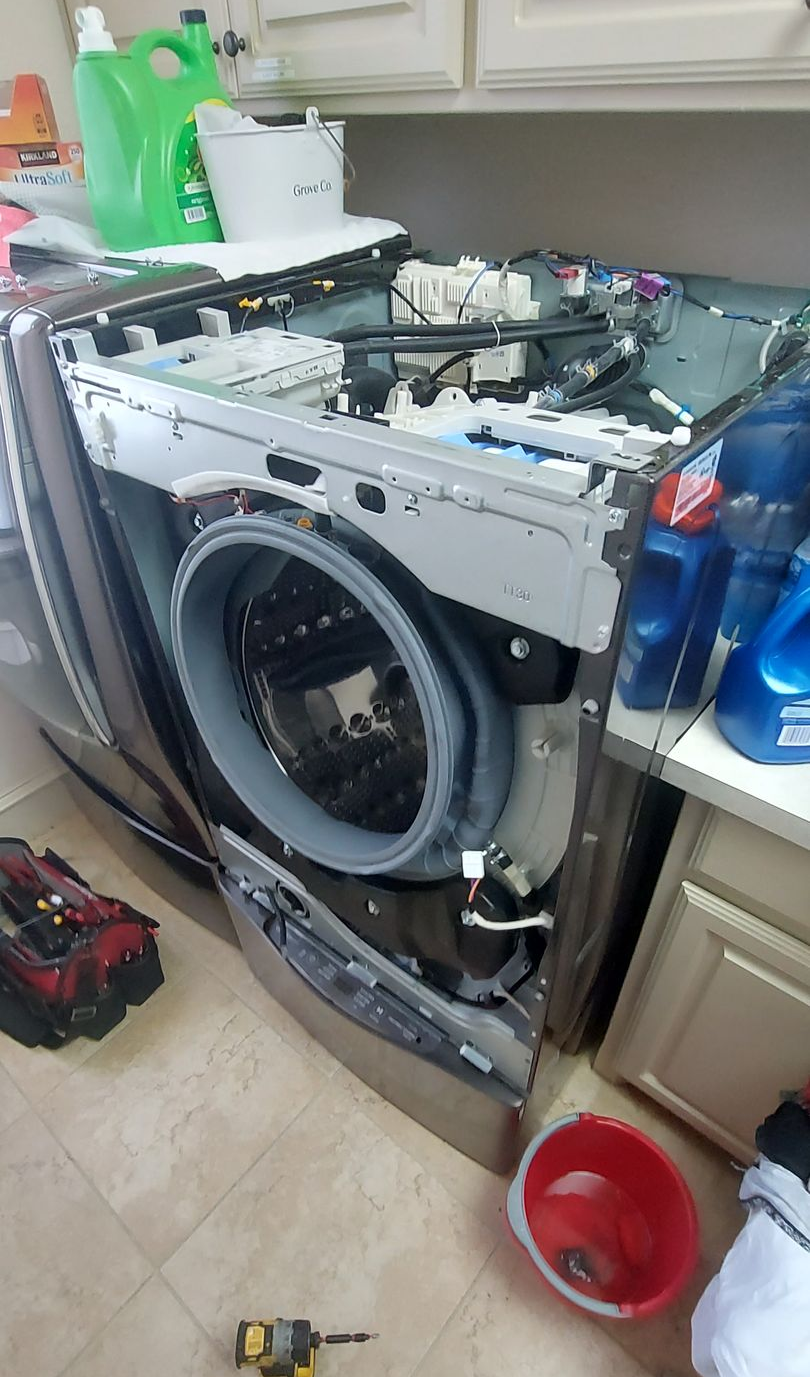 Disassembled front-load washer in a kitchen, with tools and cleaning supplies around it.