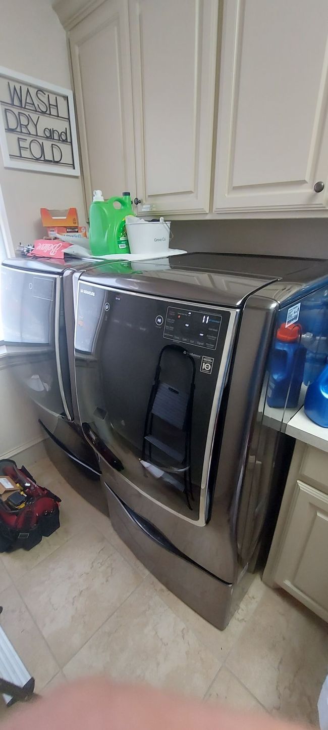 Laundry room with a front-loading washer and dryer beside white cabinets and cleaning supplies on top