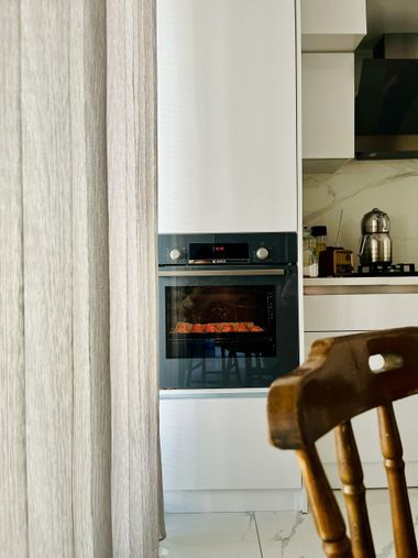 Modern kitchen with built-in oven glowing orange beside a doorway and chair in the foreground
