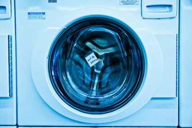 Front-loading washing machine with a round glass door in a blue-tinted laundry room