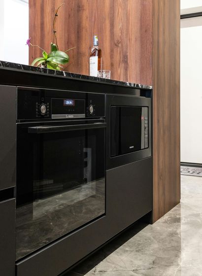 Black built-in oven with glass door beside a wood-paneled cabinet in a modern kitchen