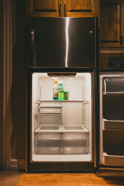 Open, mostly empty refrigerator with a few bottles on the top shelf in a kitchen
