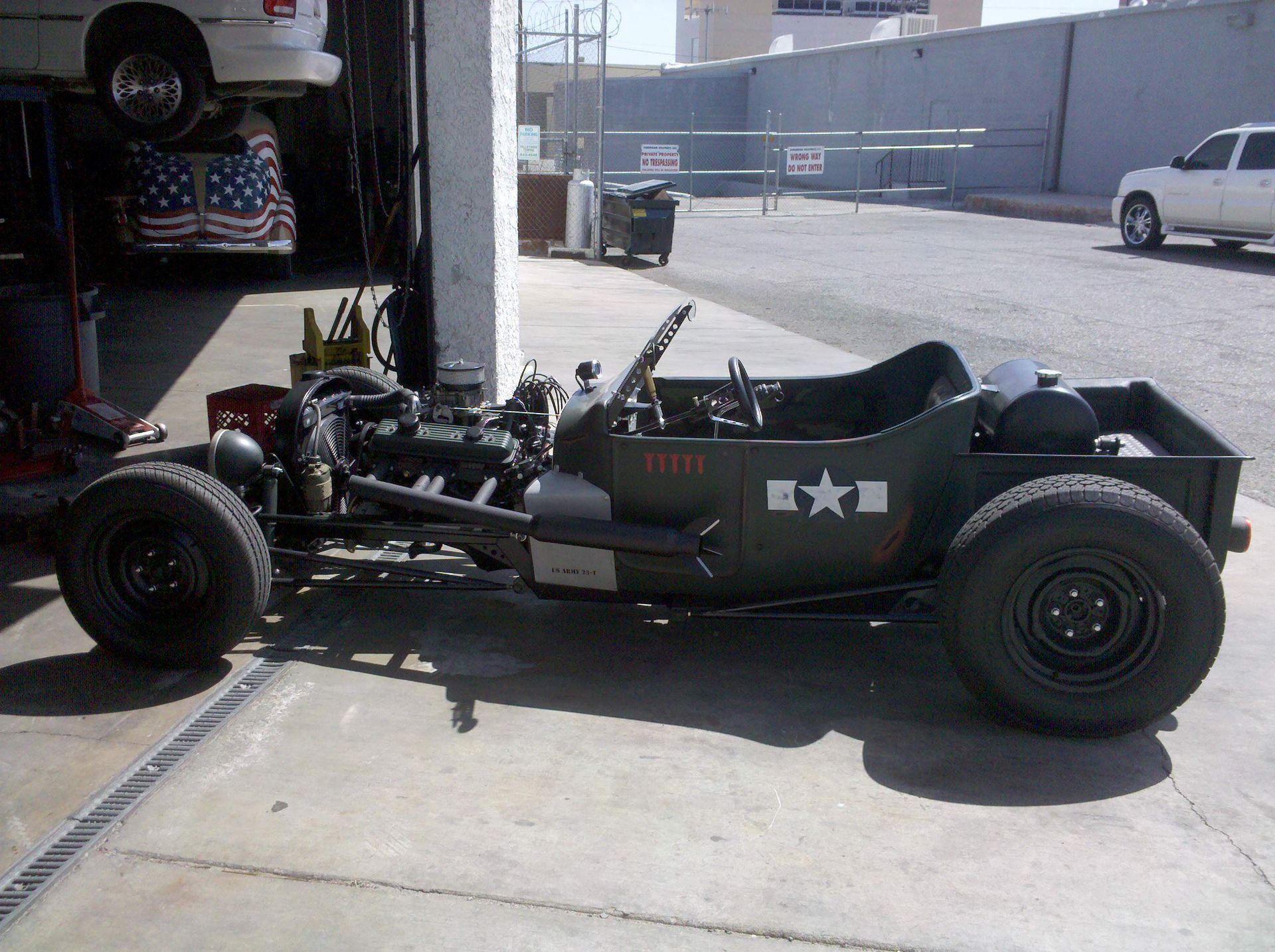 Green vintage race car parked in a driveway beside a garage, with exposed engine and white star decals