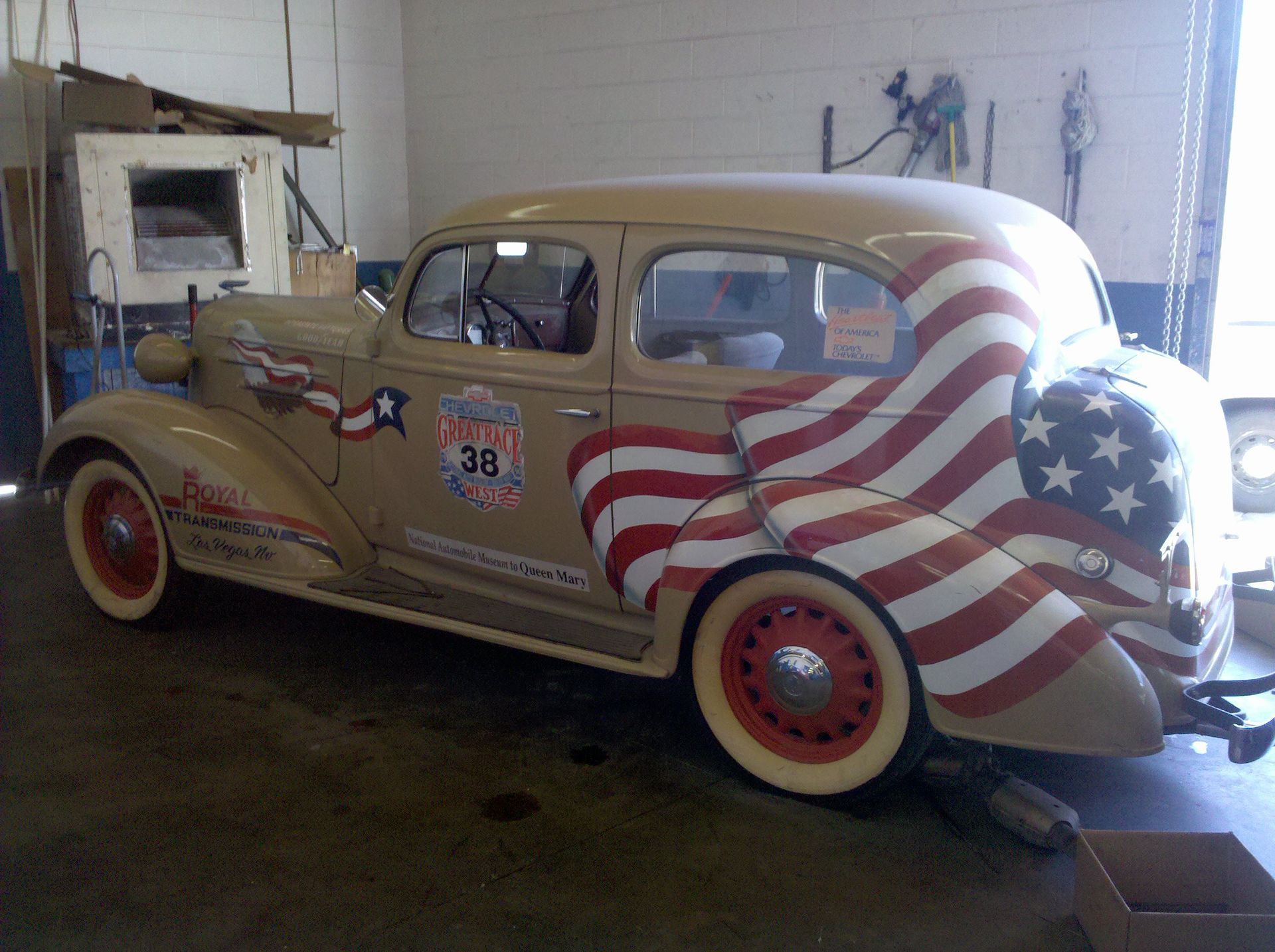 Vintage tan hot rod with red-white-and-blue patriotic swirl design parked in a garage.