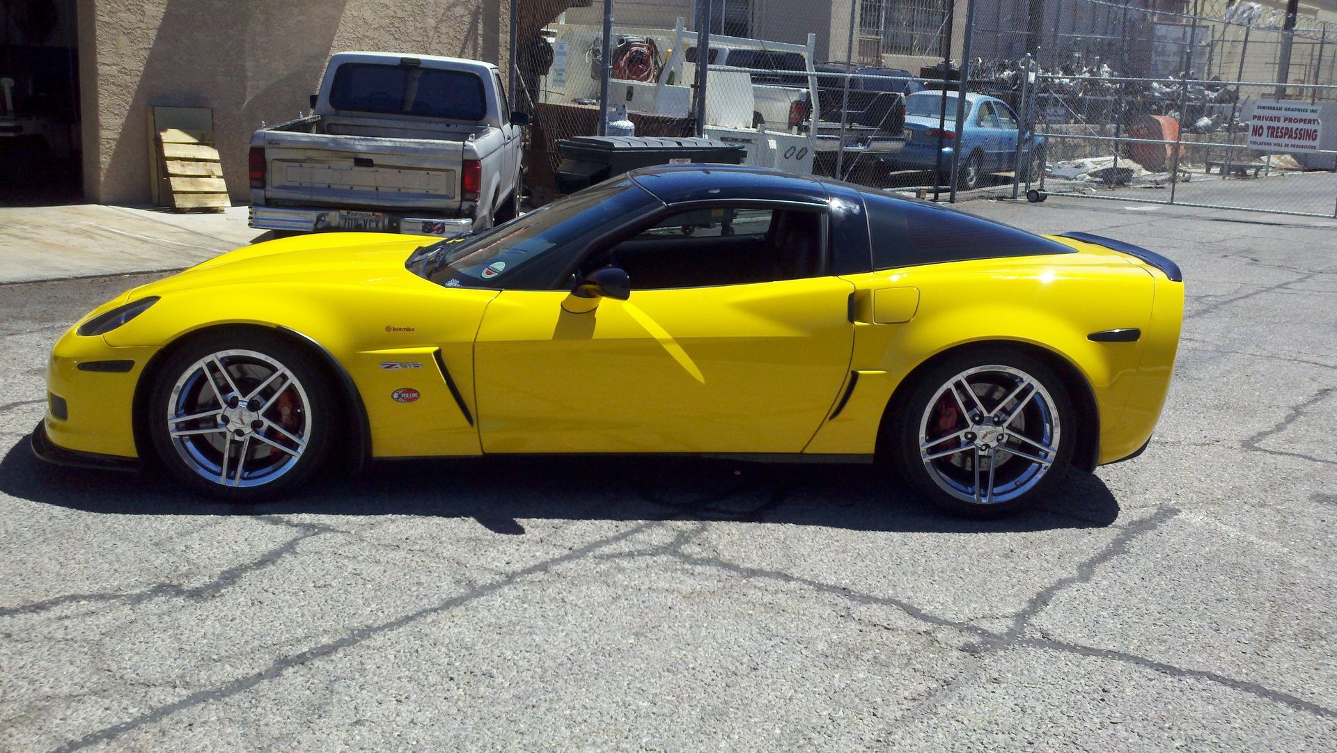 Yellow sports car parked on a cracked lot with a truck in the background
