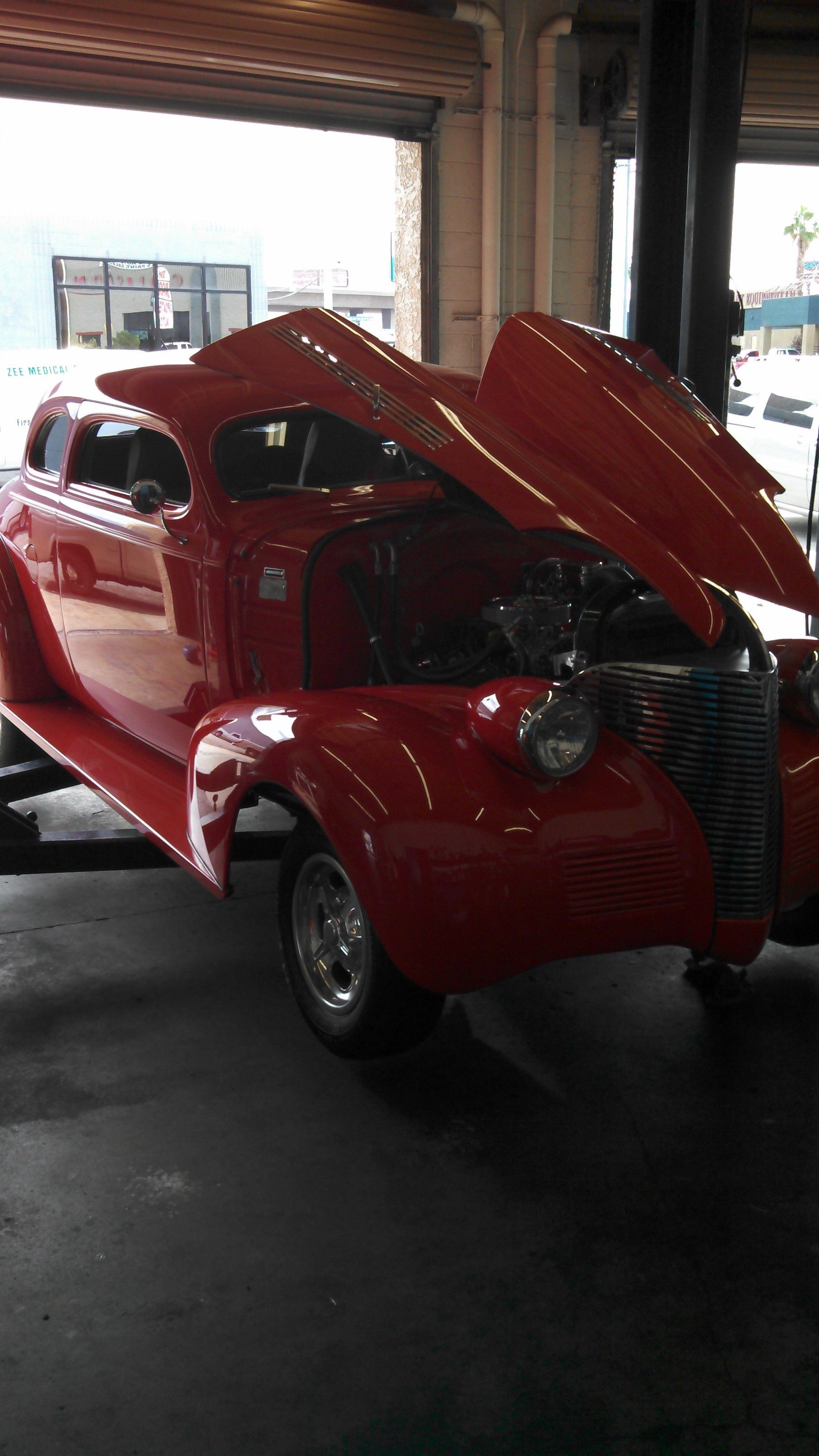 Red vintage convertible car with hood open, displayed indoors.