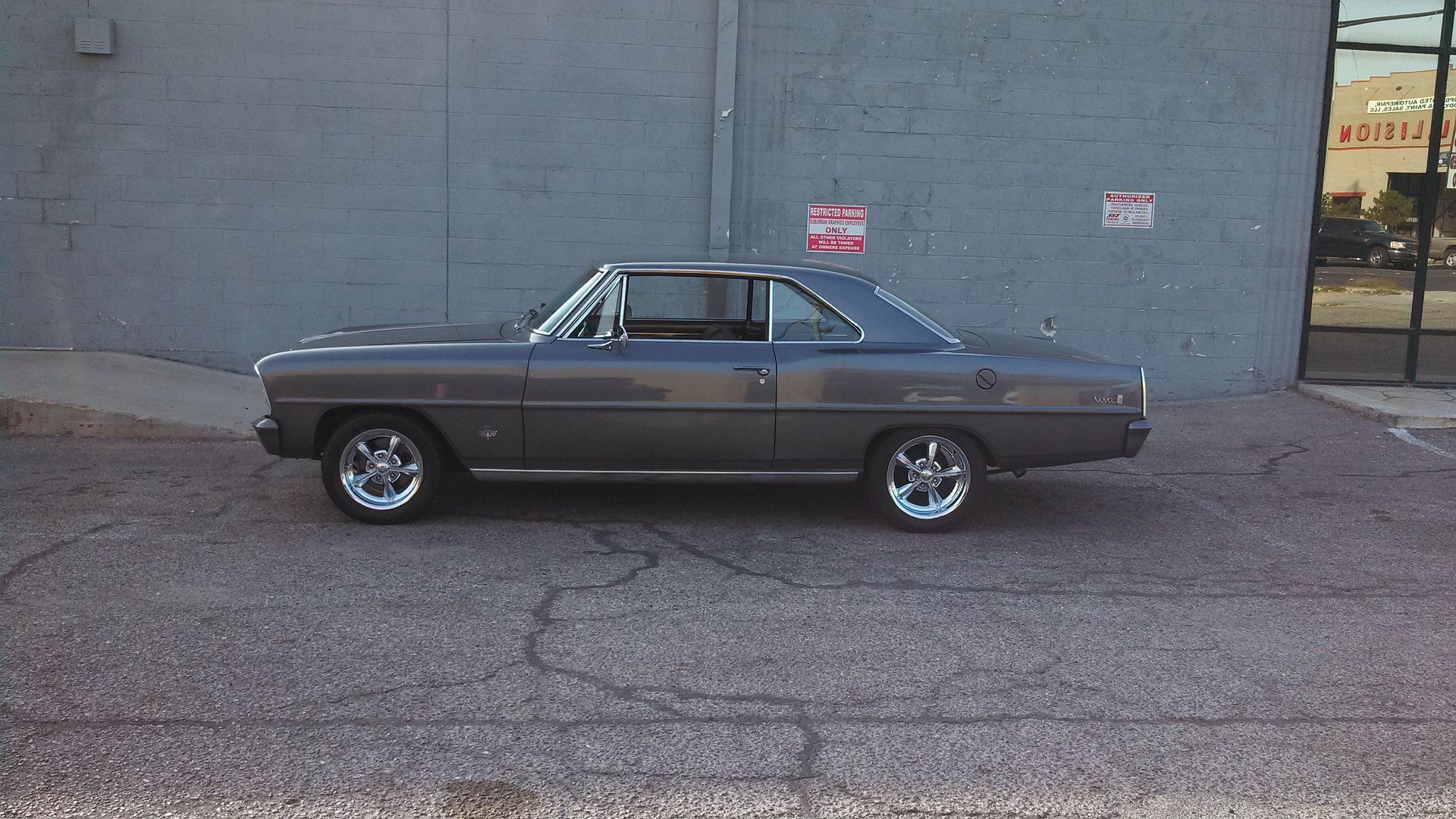 Classic brown coupe parked beside a gray wall on a paved lot