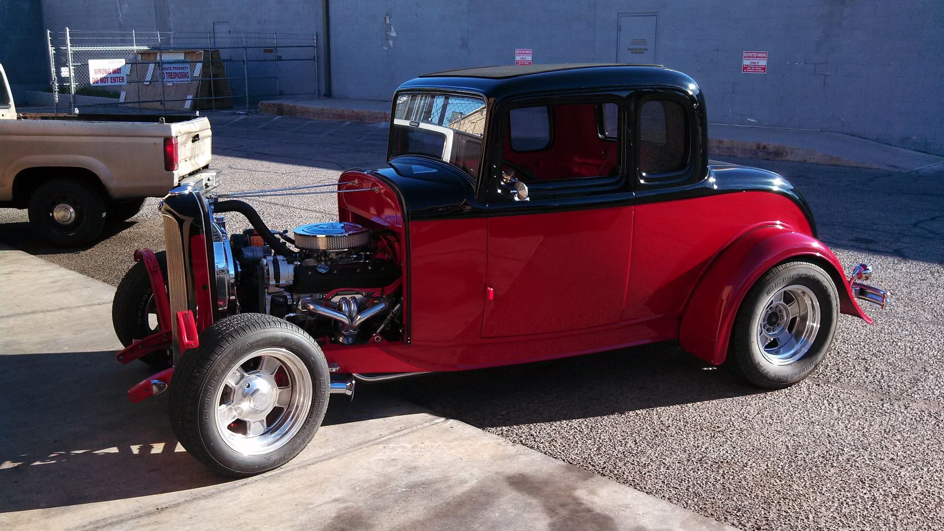 Red vintage hot rod car parked outdoors with its hood open, showing the engine.