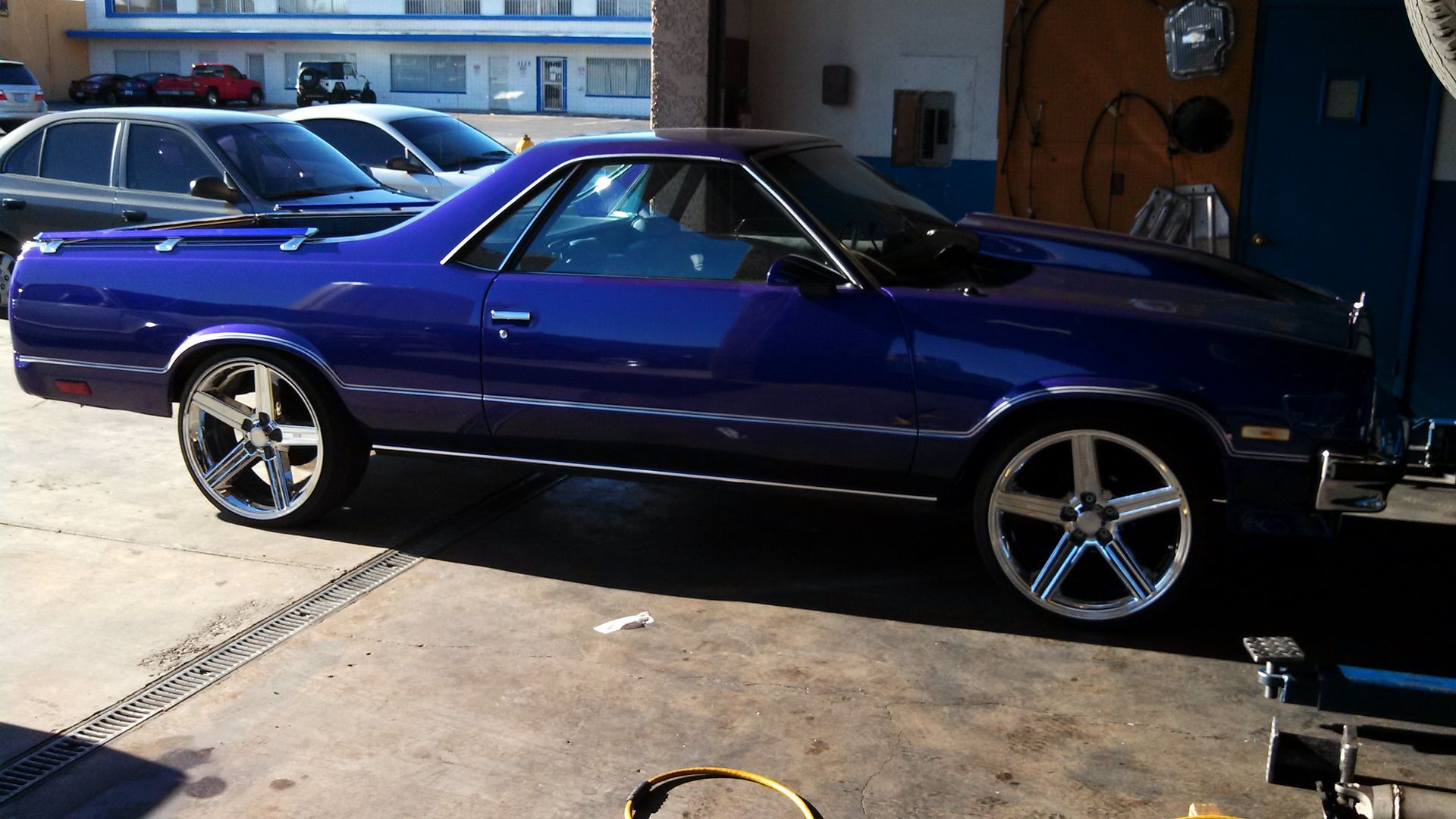 Purple classic car parked in a garage driveway, side view with chrome rims.