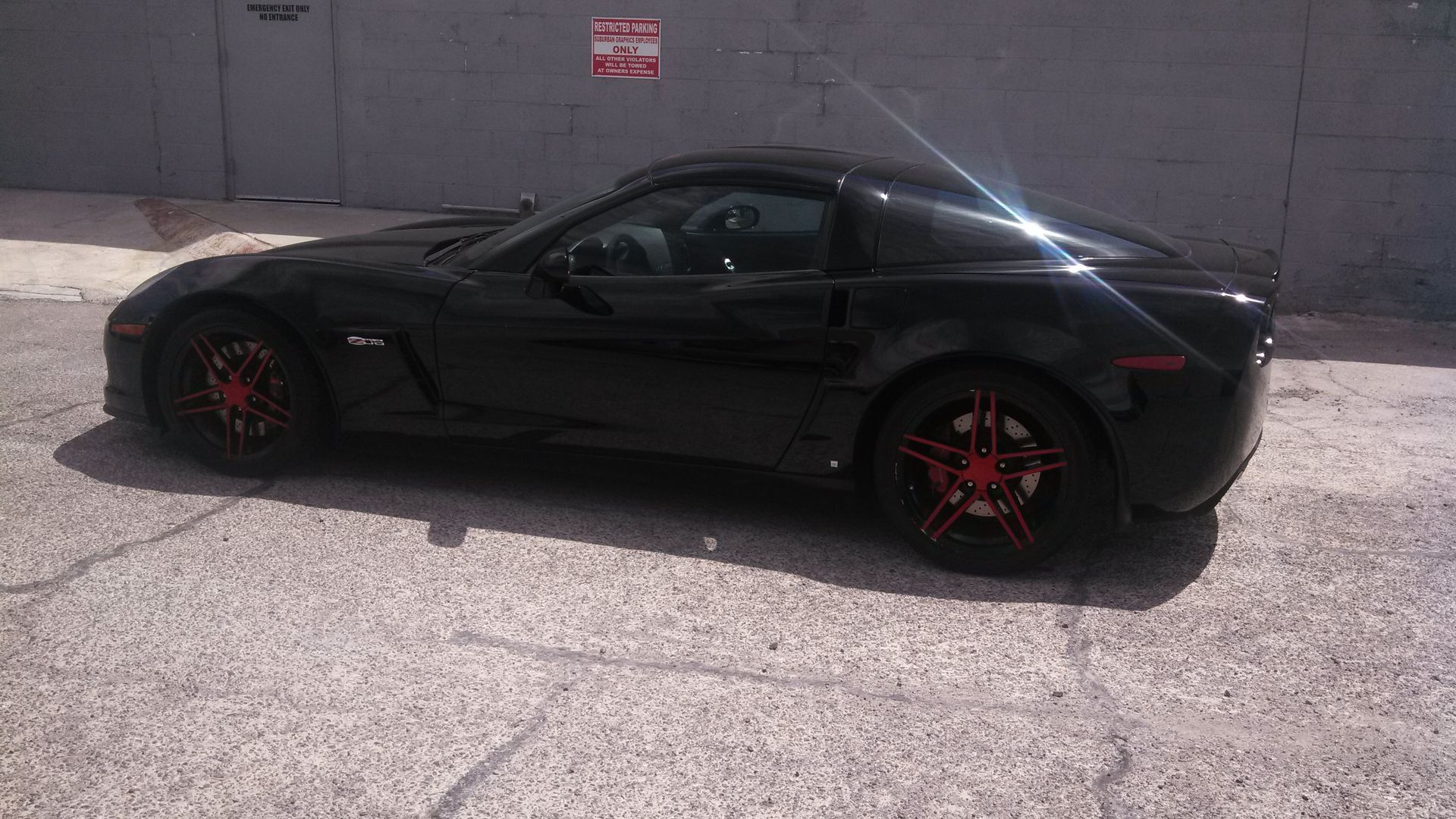 Black sports car with red rims parked beside a gray wall.