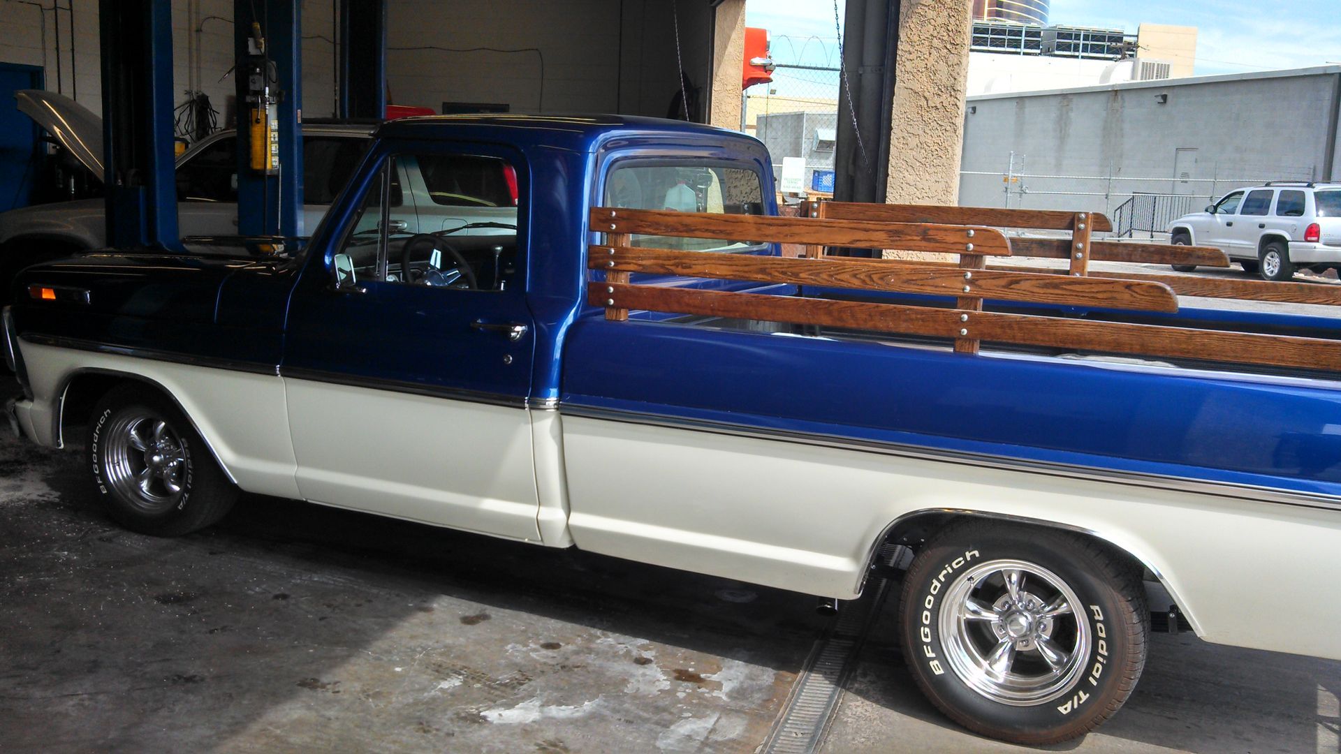 Blue and white vintage pickup truck with wooden bed rails parked indoors at a garage entrance