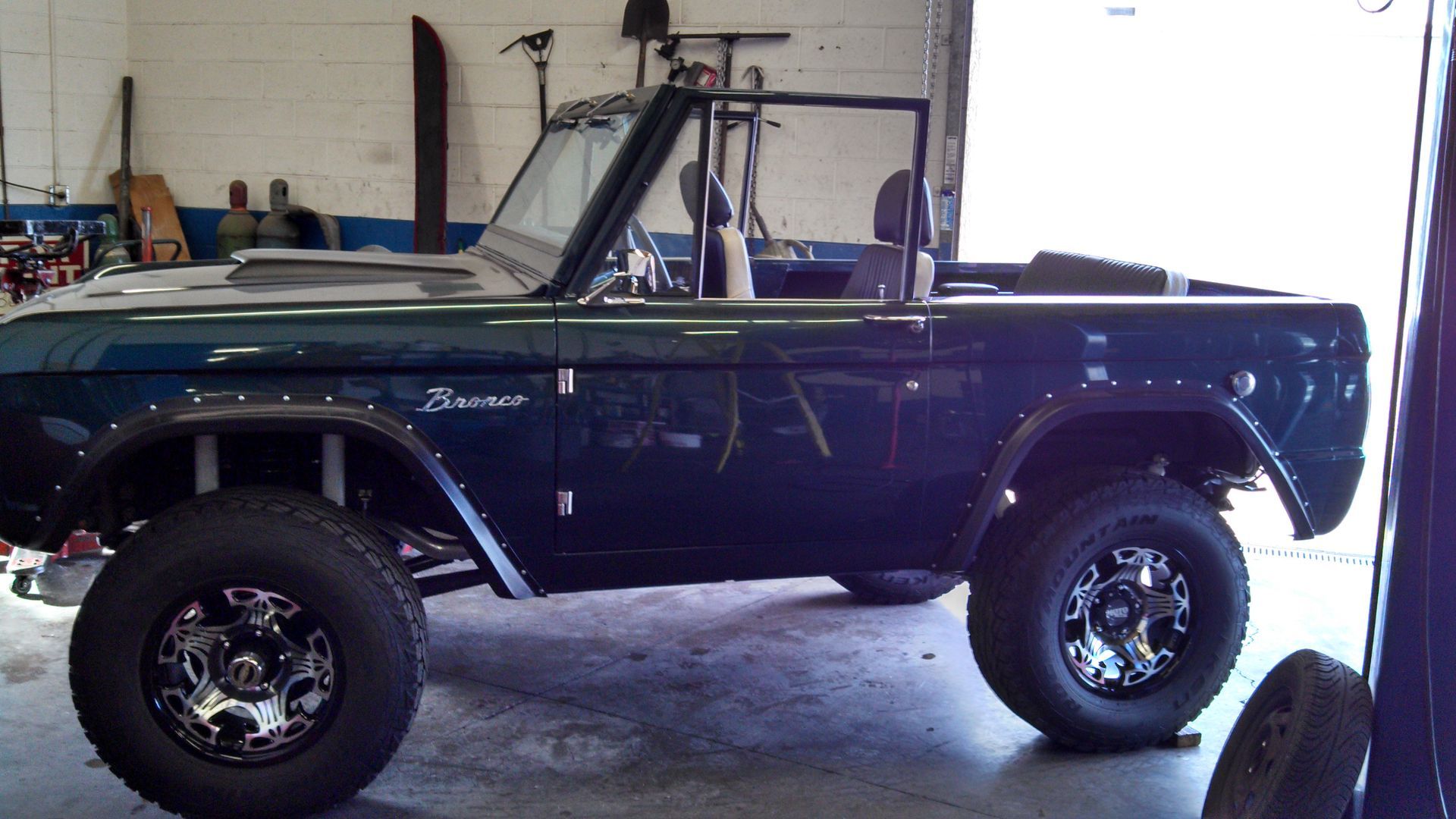 Classic blue convertible off-road truck in a garage, lifted with large black tires.