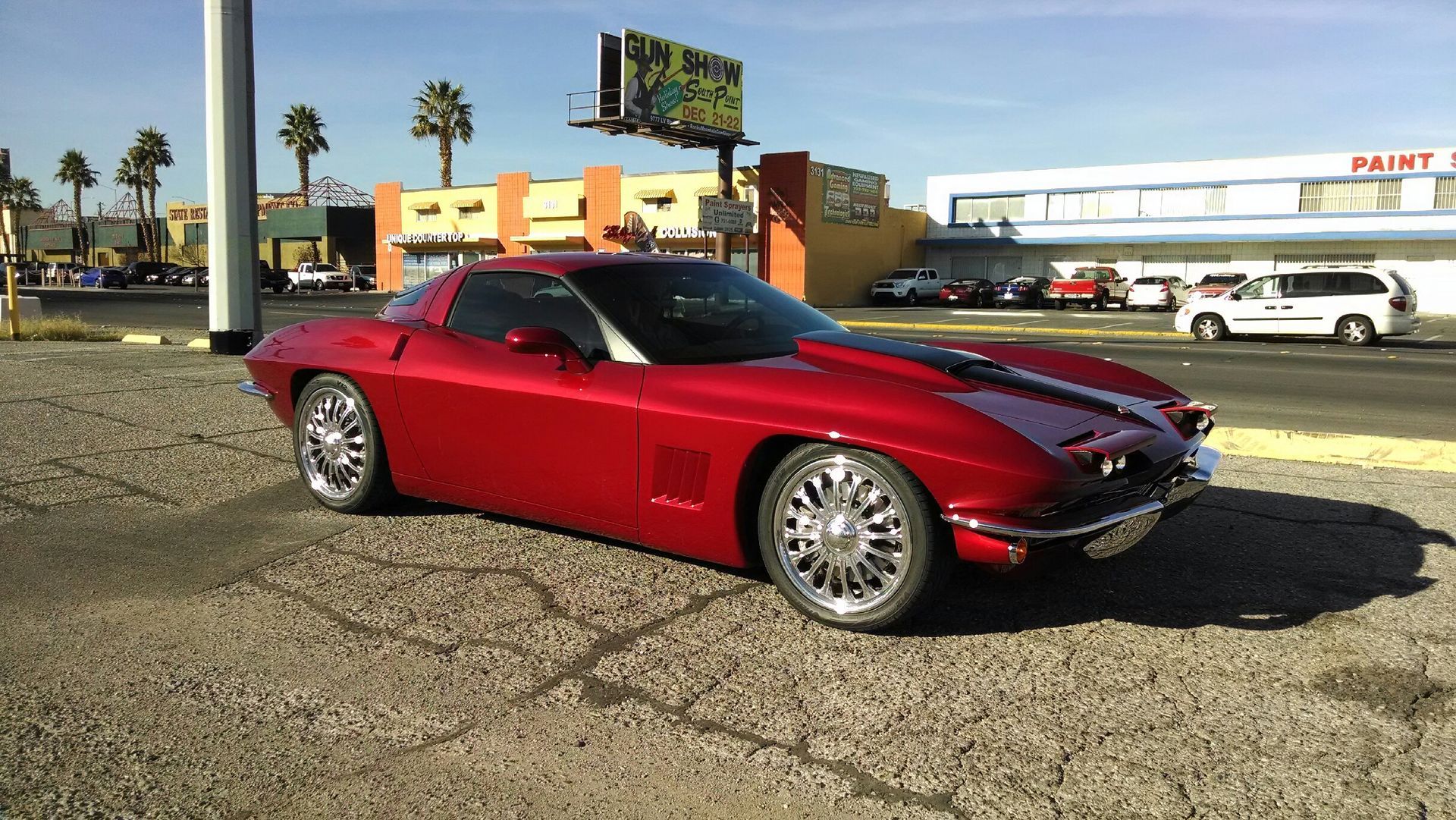 Red sports car parked on a lot in front of a storefront on a sunny day