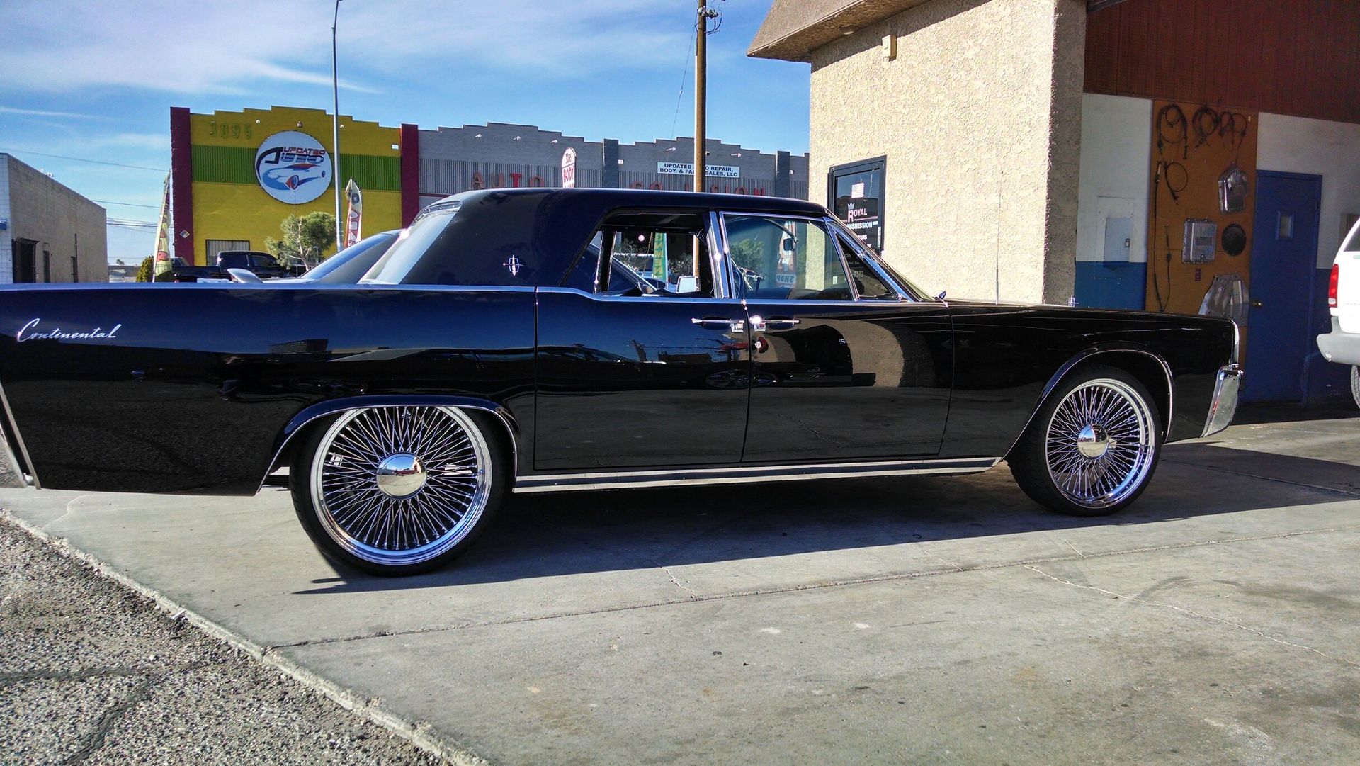 Black classic lowrider car parked outside a building in bright sunlight