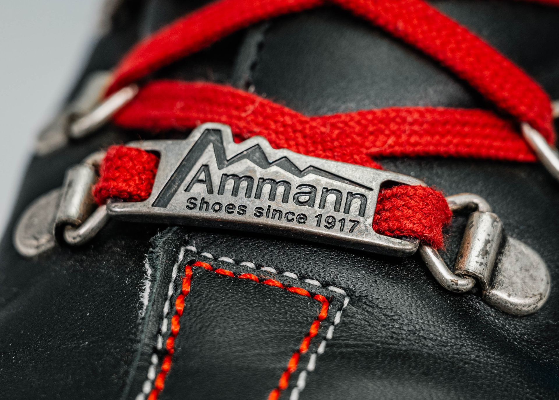 Gros plan sur une botte en cuir noir à lacets rouges. L'étiquette métallique indique « Ammann, chaussures depuis 1917 ».