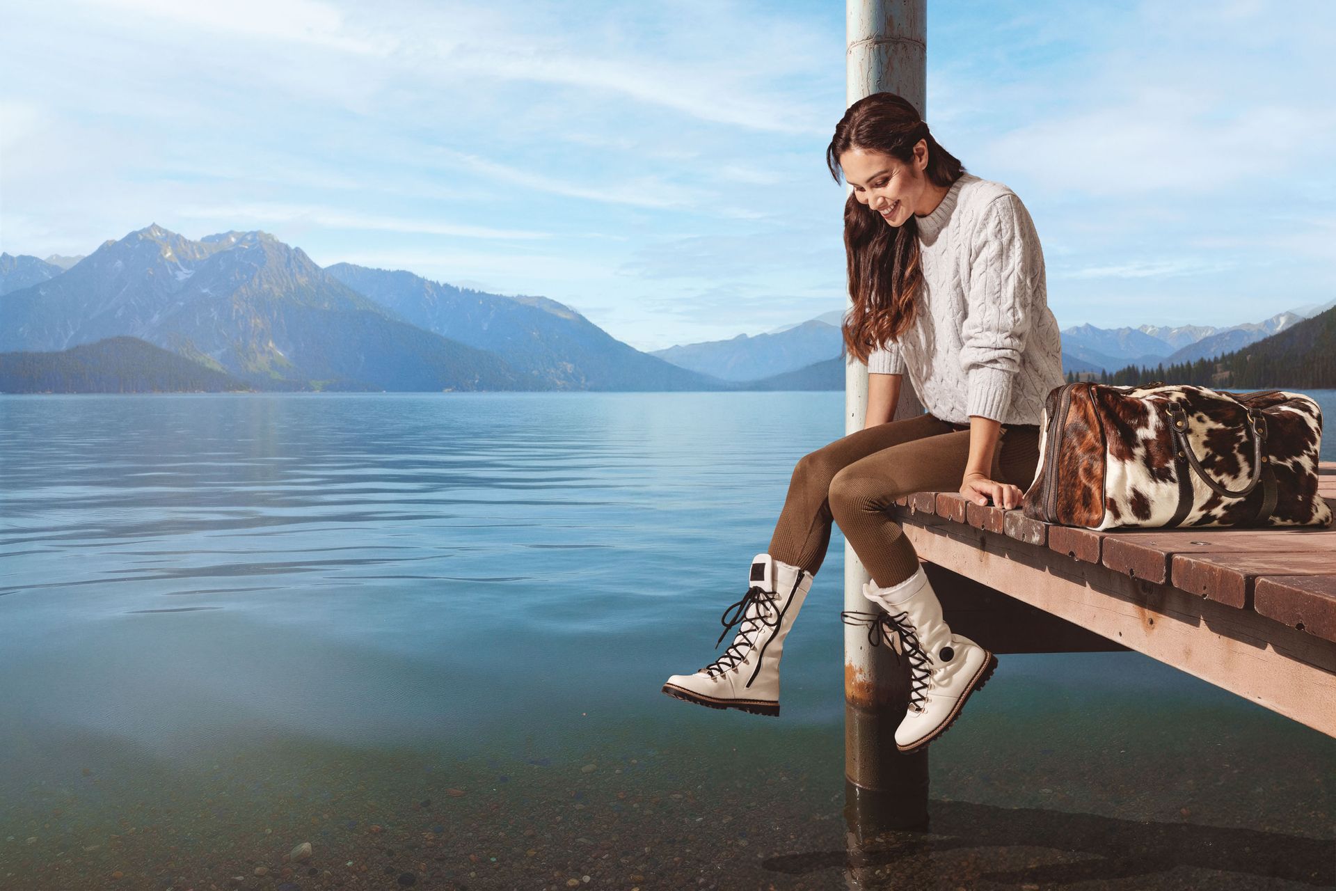 Une femme est assise sur un quai, regardant des bottes blanches, avec des montagnes et un lac en arrière-plan.