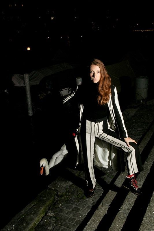 Femme en tenue rayée noire et blanche sur un quai la nuit, avec un cygne.
