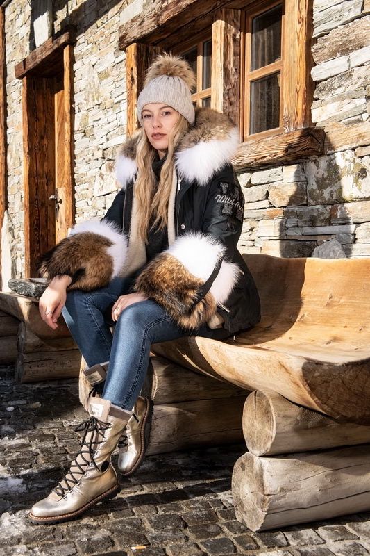 Une femme en manteau d'hiver et chapeau est assise sur un banc en bois devant un bâtiment en pierre.