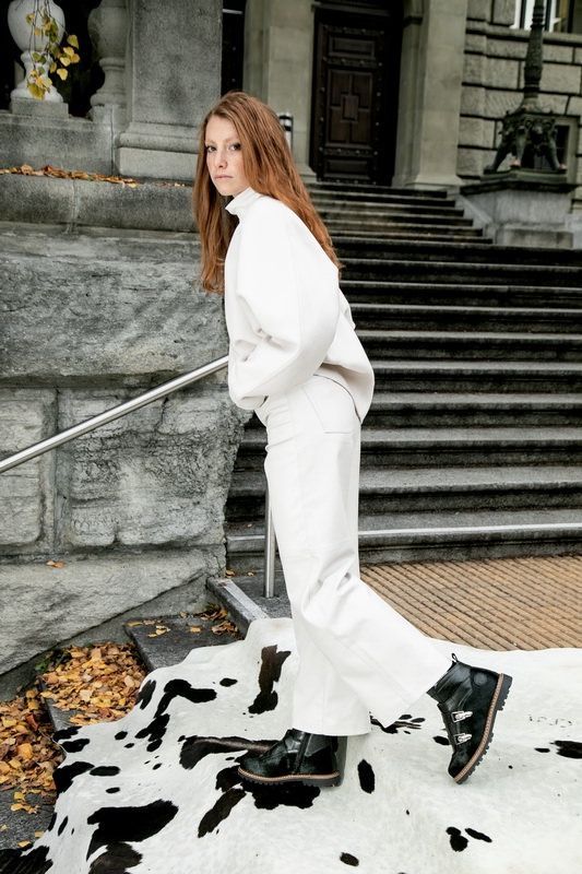 Une femme en tenue blanche et bottes noires monte les escaliers.
